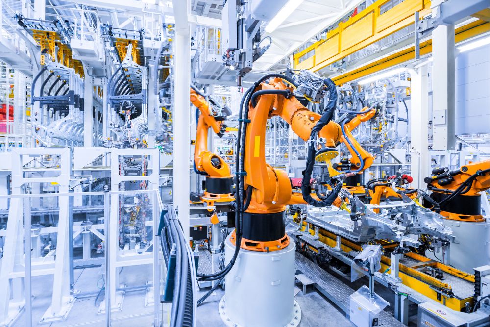 Orange industrial robot arms working on car bodies along an automated production line