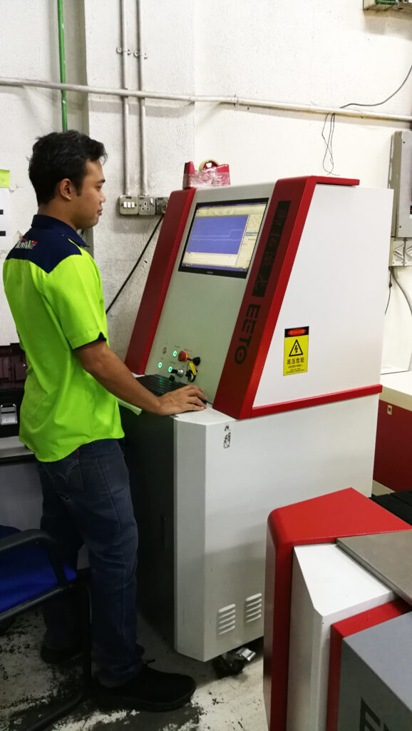 A worker in high-visibility clothing operating a panel PC mounted on factory equipment