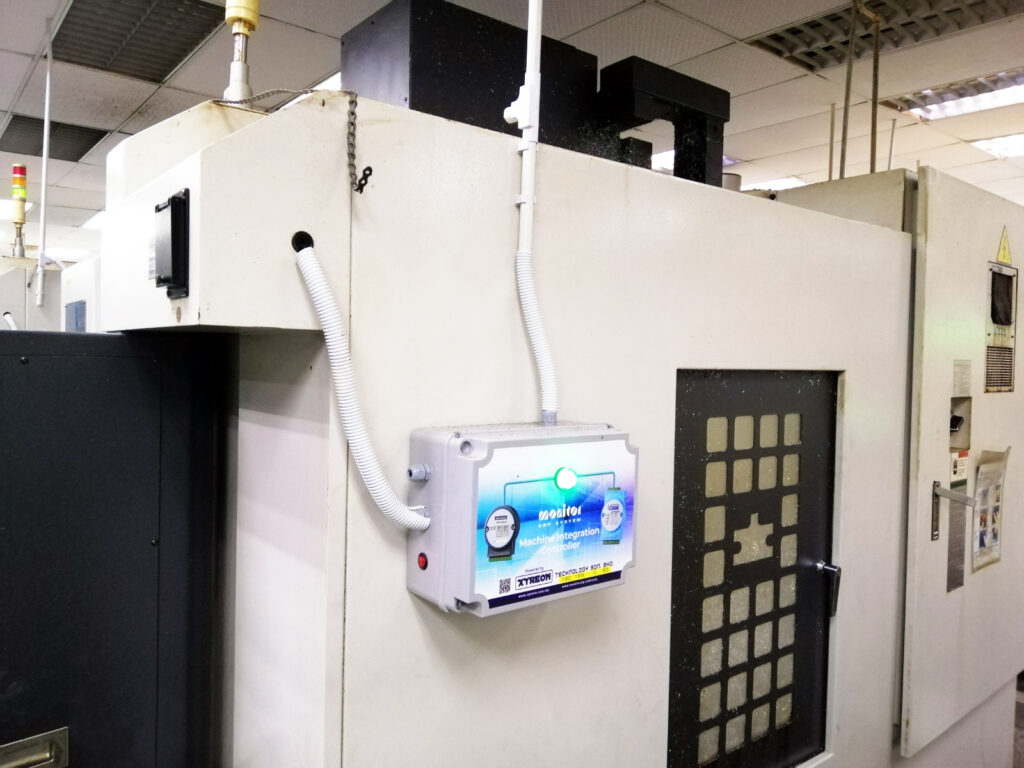 A compact industrial PC mounted on the outside of a machine enclosure on a factory floor