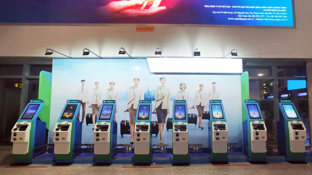A bank of self-service check-in kiosks installed along a terminal wall