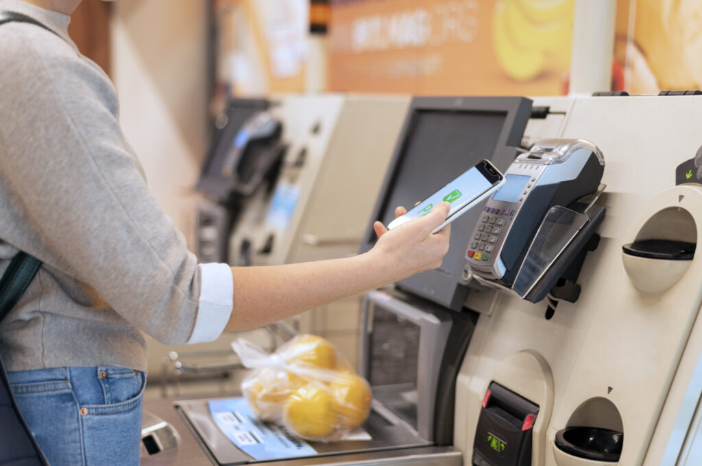 A customer holding a smartphone to the contactless reader on a self-service checkout