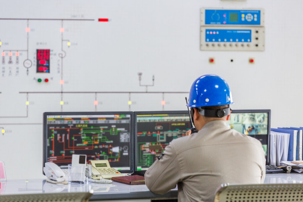 An operator in a hard hat monitoring plant systems from a control-room workstation